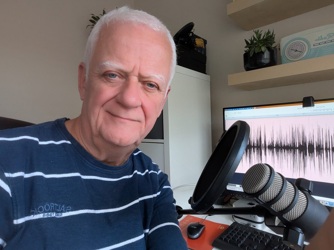 Mike Kinnaird at his podcast microphone, a recording on the screen behind him